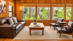 A cozy living room with a leather sofa, a wooden coffee table, and a view of a garden through large windows. - Black Butte Ranch Glaze Meadow 006 (Black Butte Ranch)