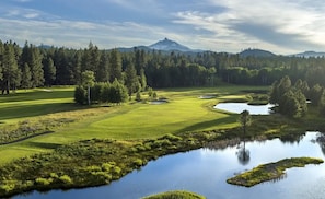 A golf course with a pond, trees, and a mountain in the background.