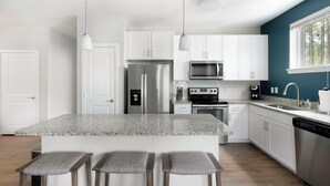 Una cocina moderna con gabinetes blancos, electrodomésticos de acero inoxidable, encimera de granito y taburetes de bar.