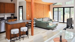 Eine moderne Küche mit Holzschränken, einer Bar und einer Sitzecke mit grünem Sofa und weißen Stühlen.
