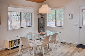A modern dining area with a glass table, white chairs, and a pendant light. - Black Butte Ranch Glaze Meadow 032 (Black Butte Ranch)