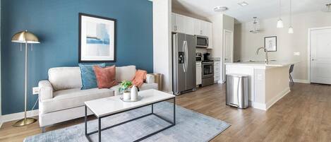 A modern living room with a sofa, coffee table, and a kitchen area with a refrigerator and stove.