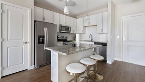 Una cocina moderna con armarios blancos, electrodomésticos de acero inoxidable, encimera de granito y una isla central con taburetes.