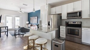 Una cocina moderna con armarios blancos, un refrigerador de acero inoxidable, un microondas, un horno e isla de granito con taburetes de bar.