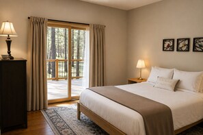 A bedroom with a large bed, two bedside lamps, a nightstand, a wooden dresser, a patterned rug, and a view of a forest through a sliding door. - Black Butte Ranch Glaze Meadow 141 (Black Butte Ranch)