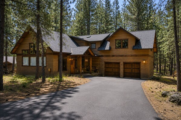 A two-story log cabin with a covered porch, a garage, and a paved driveway. - Black Butte Ranch Glaze Meadow 141 (Black Butte Ranch)
