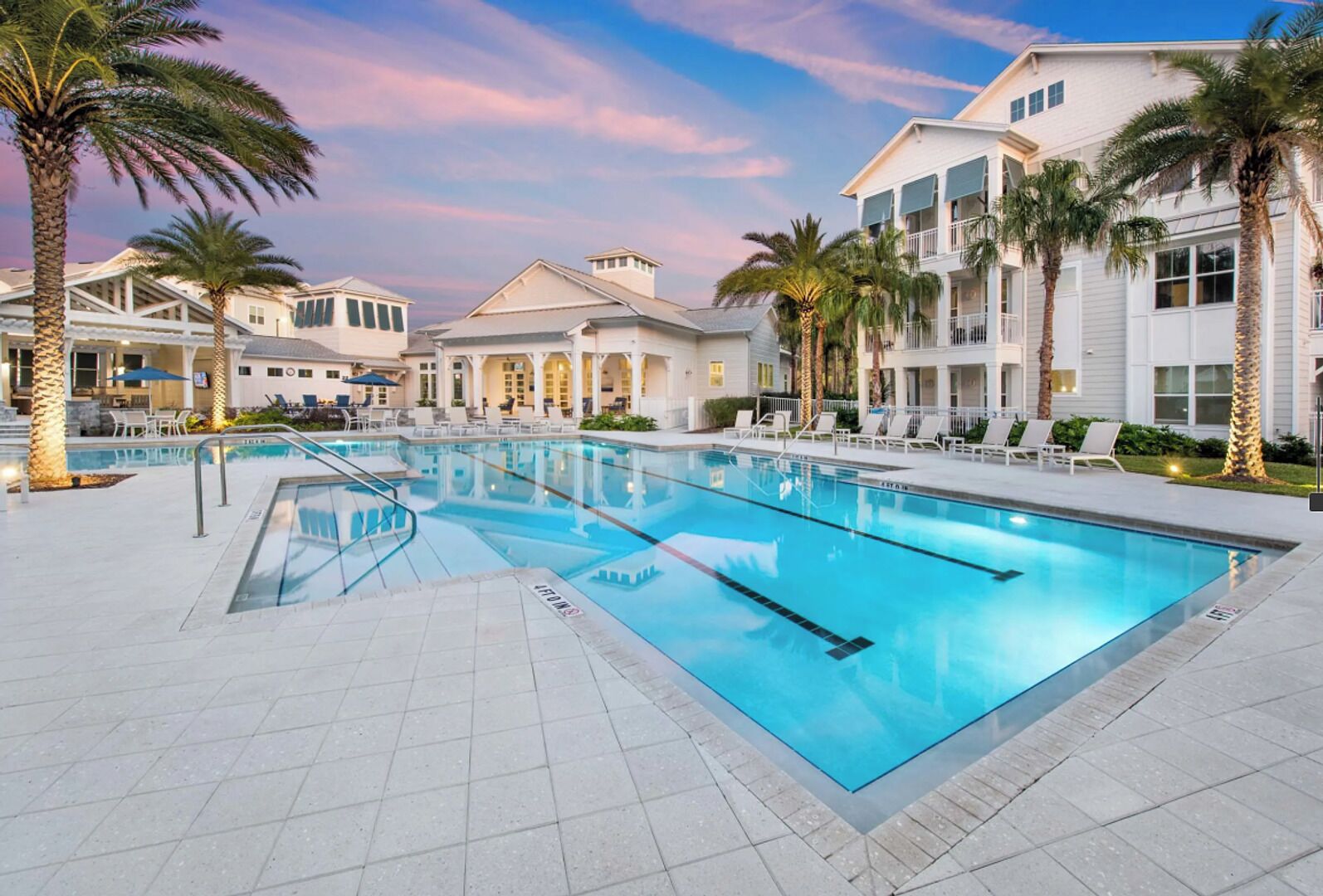 A swimming pool with lounge chairs and palm trees, surrounded by buildings with balconies.