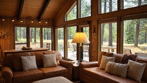 Een gezellig cabin interieur met een leren bank, een kleine tafel en een lamp. Grote ramen bieden uitzicht op het omliggende bos.