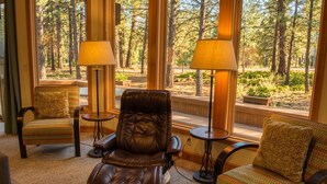 Une pièce comprenant un fauteuil en cuir, deux fauteuils à motifs et une fenêtre donnant sur une forêt.