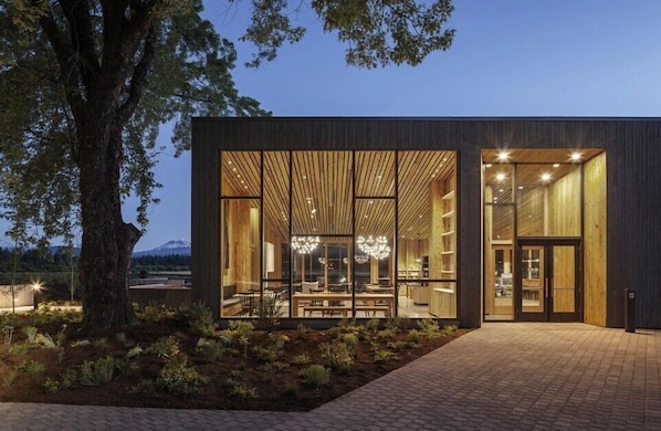 Un edificio moderno con amplios ventanales, un sendero de ladrillo y un árbol en primer plano.