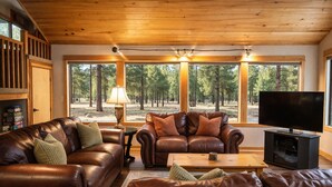 A cozy cabin interior with leather sofas, a television, and large windows offering a forest view. - Black Butte Ranch Glaze Meadow 399 (Black Butte Ranch)