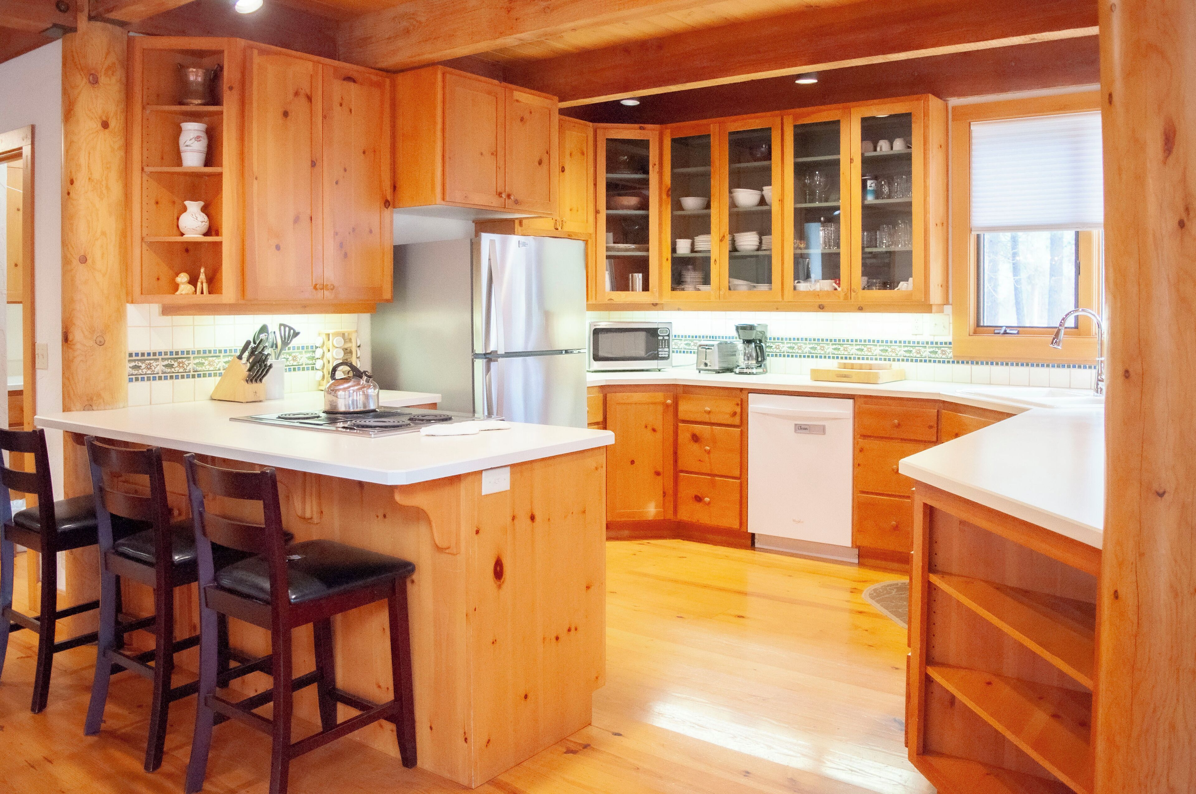 A wooden kitchen with a central island, bar stools, and a microwave.