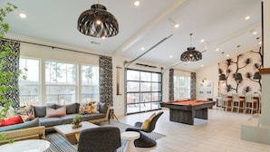 Amplia sala de estar con mesa de billar, asientos cómodos y grandes ventanales con vistas al exterior.