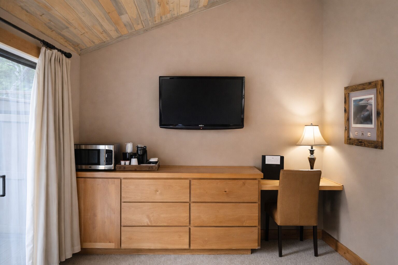 Une pièce de taille modeste, dotée d’un bureau en bois, d’un téléviseur fixé au mur, d’une chaise, d’une machine à café et d’un four à micro-ondes.