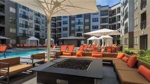 Un espace aménagé au bord de la piscine, avec des chaises longues et un foyer, entouré d’un immeuble à plusieurs étages doté de balcons.