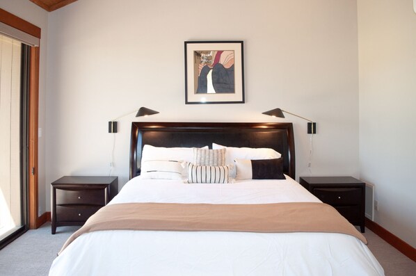 A bedroom with a large bed, two bedside tables, a framed picture on the wall, and a window with blinds. - Black Butte Ranch Lodge Room 015 (Black Butte Ranch)