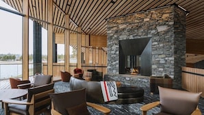 Un salon moderne avec des murs en pierre, un plafond en bois et de grandes fenêtres donnant sur une étendue d’eau.