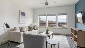 Een moderne woonkamer met een bank, fauteuil, salontafel en een aan de muur bevestigde televisie.