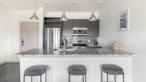 Een moderne keuken met een groot eiland, roestvrijstalen apparatuur, hanglampen en een backsplash met een herringbone-patroon.