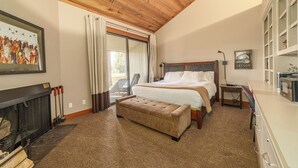 Een slaapkamer met een groot bed, een houten plafond, een open haard en uitzicht op de omgeving.