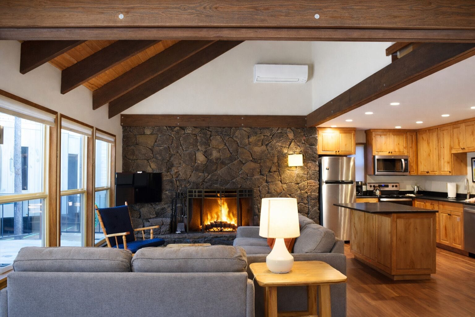 A modern living room with a stone fireplace, a sofa, a lamp, and a view of the outside through large windows.