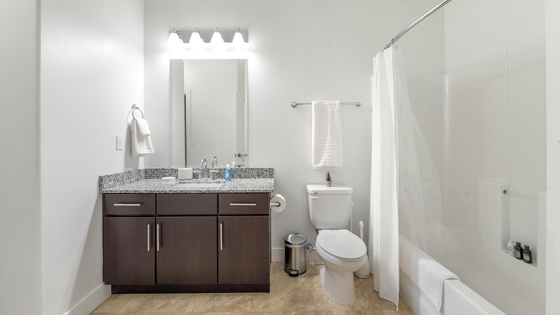 A modern bathroom with a dark wood vanity, a white toilet, and a walk-in shower with a glass door.