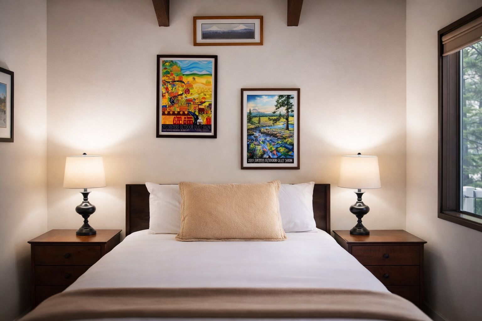 A hotel room with a bed, two bedside tables, two lamps, and two framed posters on the wall.