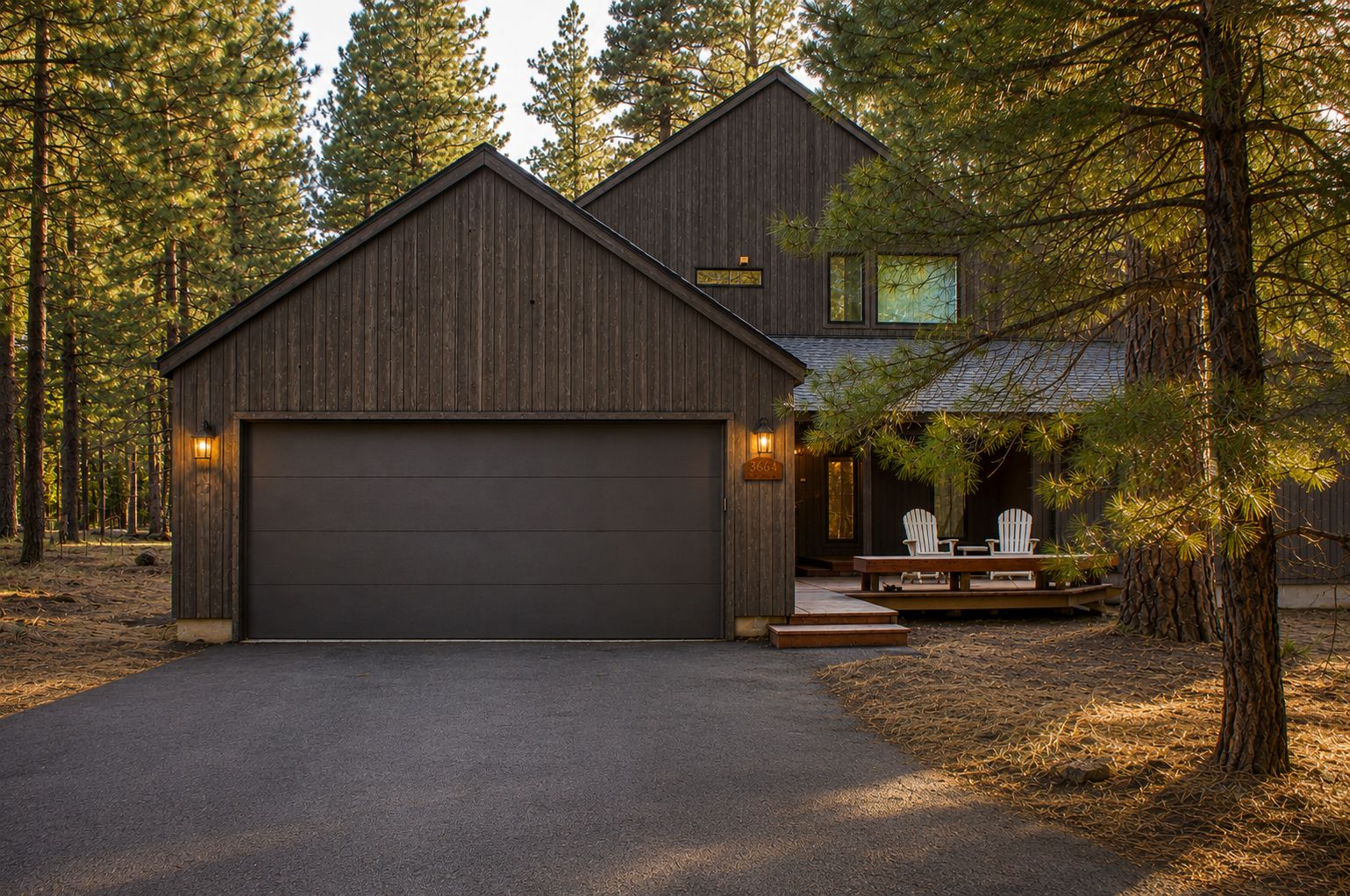 A two-story wooden house with a garage, surrounded by trees.