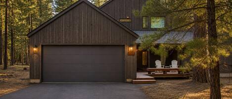 A two-story wooden house with a garage, surrounded by trees.