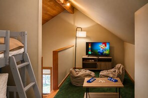 A cozy attic room with a bunk bed, a television, a desk with board games, and a window. - Black Butte Ranch Ranch House 002 (Black Butte Ranch)