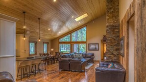 A spacious living area with a wooden ceiling, stone accent wall, and large windows offering a view of the outdoors. - Black Butte Ranch Rock Ridge 004 (Black Butte Ranch)
