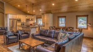 A spacious living area with a leather sofa, a wooden coffee table, and a kitchen with white cabinets and stainless steel appliances. - Black Butte Ranch Rock Ridge 004 (Black Butte Ranch)