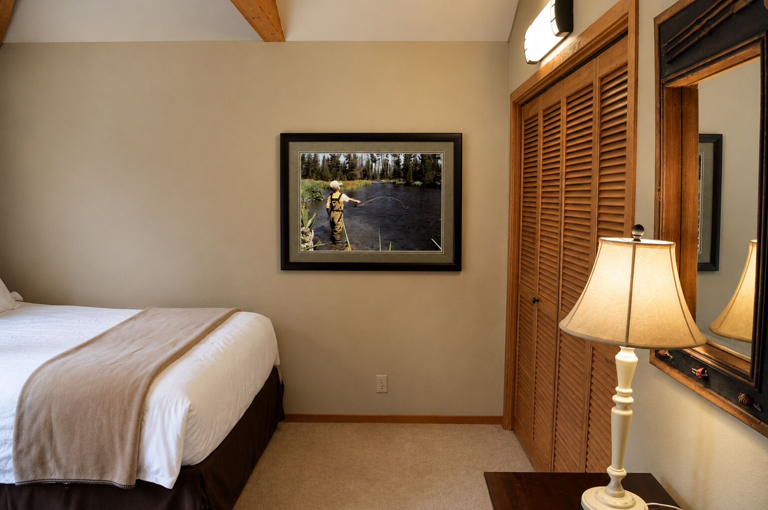 A bedroom with a bed, a framed photograph on the wall, a wooden wardrobe, and a bedside lamp.