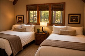 A bedroom with two beds, a nightstand with a lamp, framed pictures, and a window with blinds.