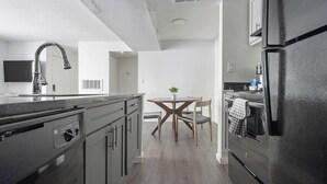 A modern kitchen with grey cabinetry, a stainless steel refrigerator, and a wooden dining table with chairs. - Landing | Incredible 2BD, Gym, Clubhouse (Winston-Salem)