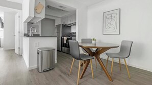 A modern kitchen with stainless steel appliances, a dining area with a round table and two chairs, and a trash bin.