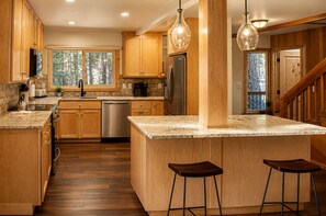 A kitchen with wooden cabinets, a stainless steel refrigerator, a dishwasher, and a large island with stools.