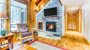 A spacious living area with a stone fireplace, wooden floors, and a large window.