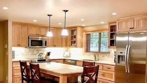 A kitchen with wooden cabinets, a stainless steel refrigerator, a microwave, and pendant lights.