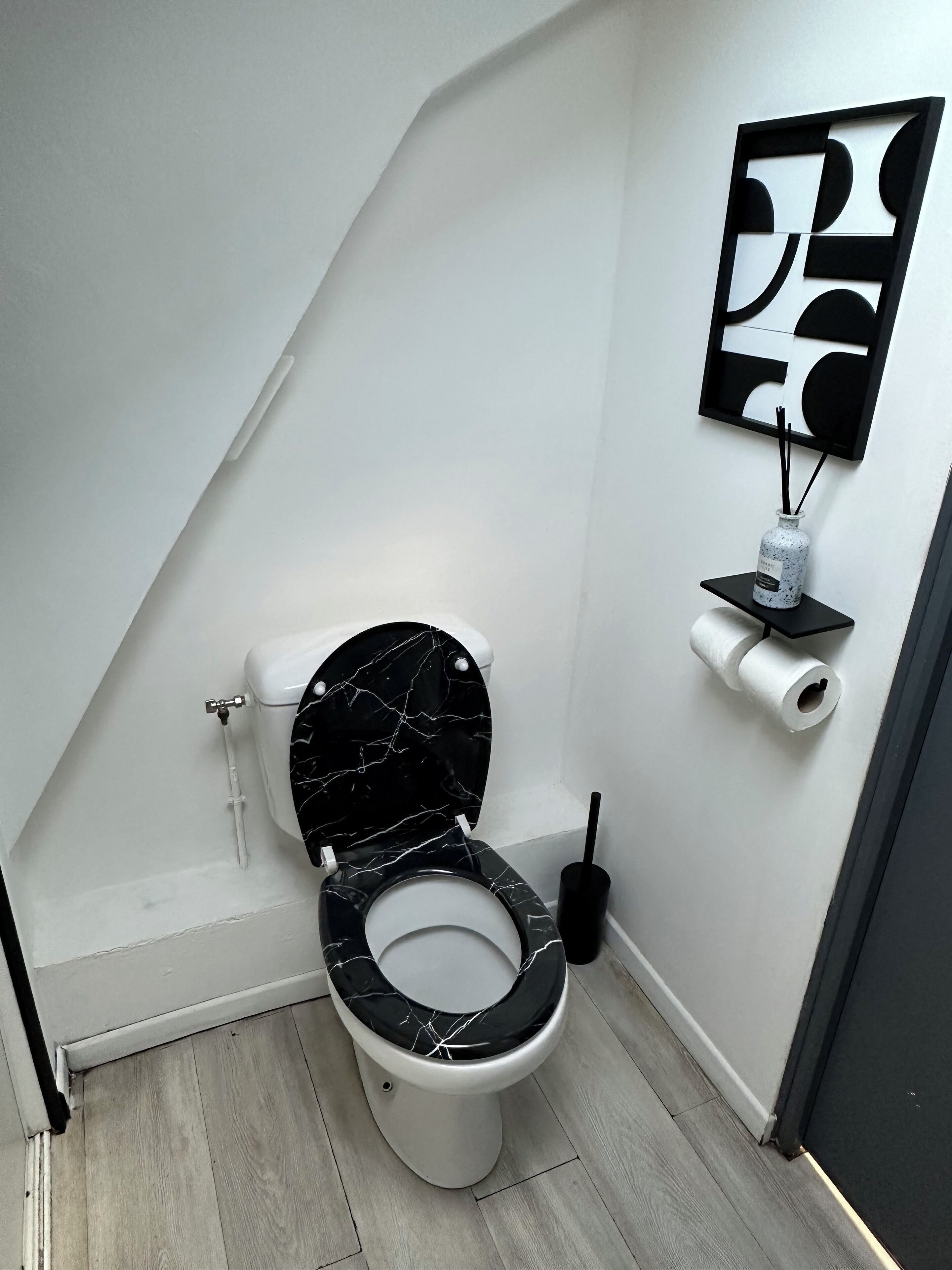 A modern bathroom with a black marble toilet, a toilet paper holder, and a black wall-mounted shelf with a bottle and reed diffuser.