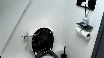 A modern bathroom with a black marble toilet, a toilet paper holder, and a black wall-mounted shelf with a bottle and reed diffuser.