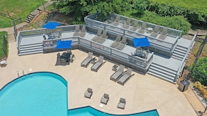 A rooftop pool area with lounge chairs and umbrellas, surrounded by a wooden deck and a swimming pool.