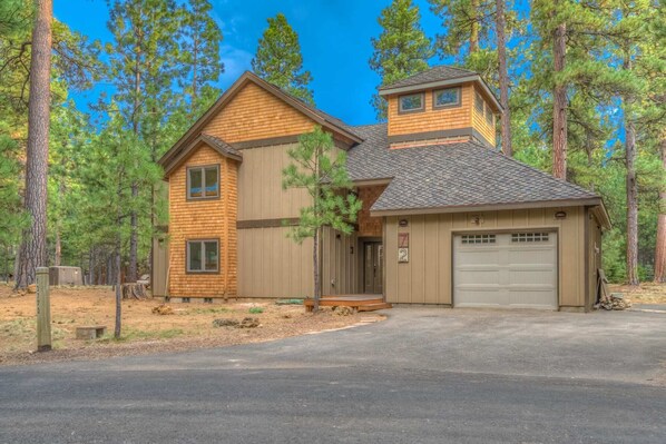 A two-story wooden house with a garage, surrounded by tall pine trees. - Black Butte Ranch South Meadow 072 (Black Butte Ranch)