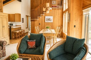 A spacious living area with a dining table, two green upholstered chairs, a wooden staircase, and a kitchen area with wooden cabinets. - Black Butte Ranch South Meadow 090 (Black Butte Ranch)