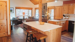 A spacious kitchen with wooden cabinets, a central island with stools, and a dining area with a sofa and chairs. - Black Butte Ranch South Meadow 098 (Black Butte Ranch)
