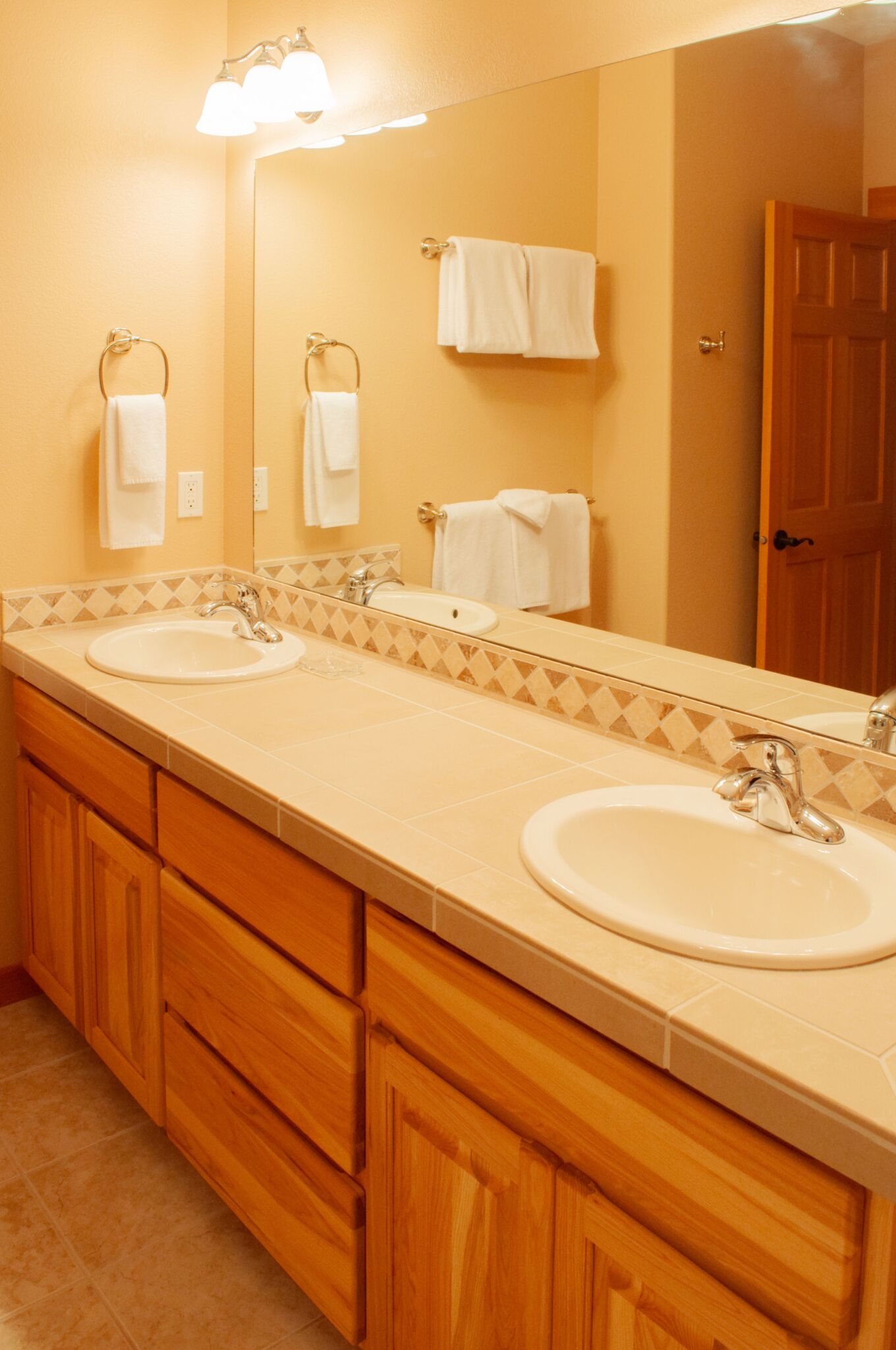 A bathroom with two sinks, wooden cabinets, a large mirror, and a door.