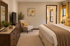 A bedroom with a bed, a chair, a dresser, a television, and artwork on the wall.