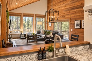 A modern kitchen with a marble countertop, a built-in sink, and a dining area with a wooden table and chairs. - Black Butte Ranch South Meadow 139 (Black Butte Ranch)