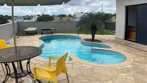 A swimming pool with a stone deck, a table with chairs, and an umbrella. - Pet-friendly country house We accept pets of all sizes 🐾🐾 (Paranapanema)