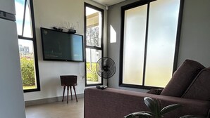A modern living room with a large window, a flat-screen TV mounted on the wall, a sofa, a small table, and a potted plant. - Pet-friendly country house We accept pets of all sizes 🐾🐾 (Paranapanema)